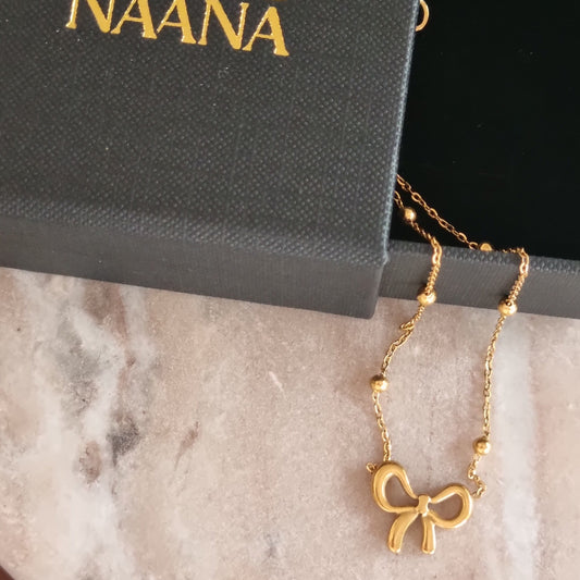 Gold necklace with a bow charm on a Doly And Nana branded box.