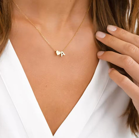 Gold necklace with a heart and letter 'A' pendant worn by a person in a white top.