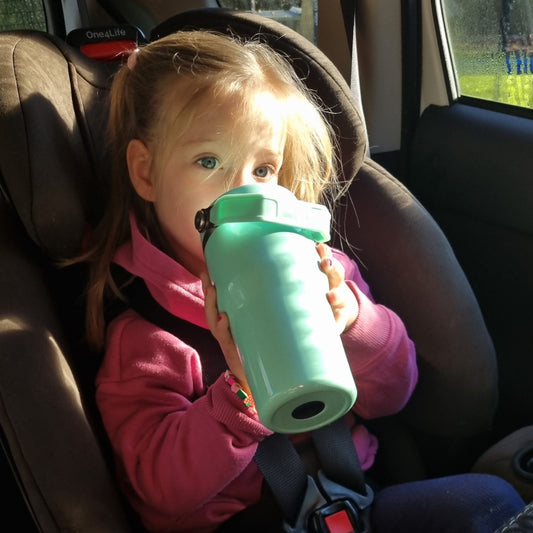Child in a car seat holding a Mint insulated stainless steel drink bottle for kids – Dolly & Naana