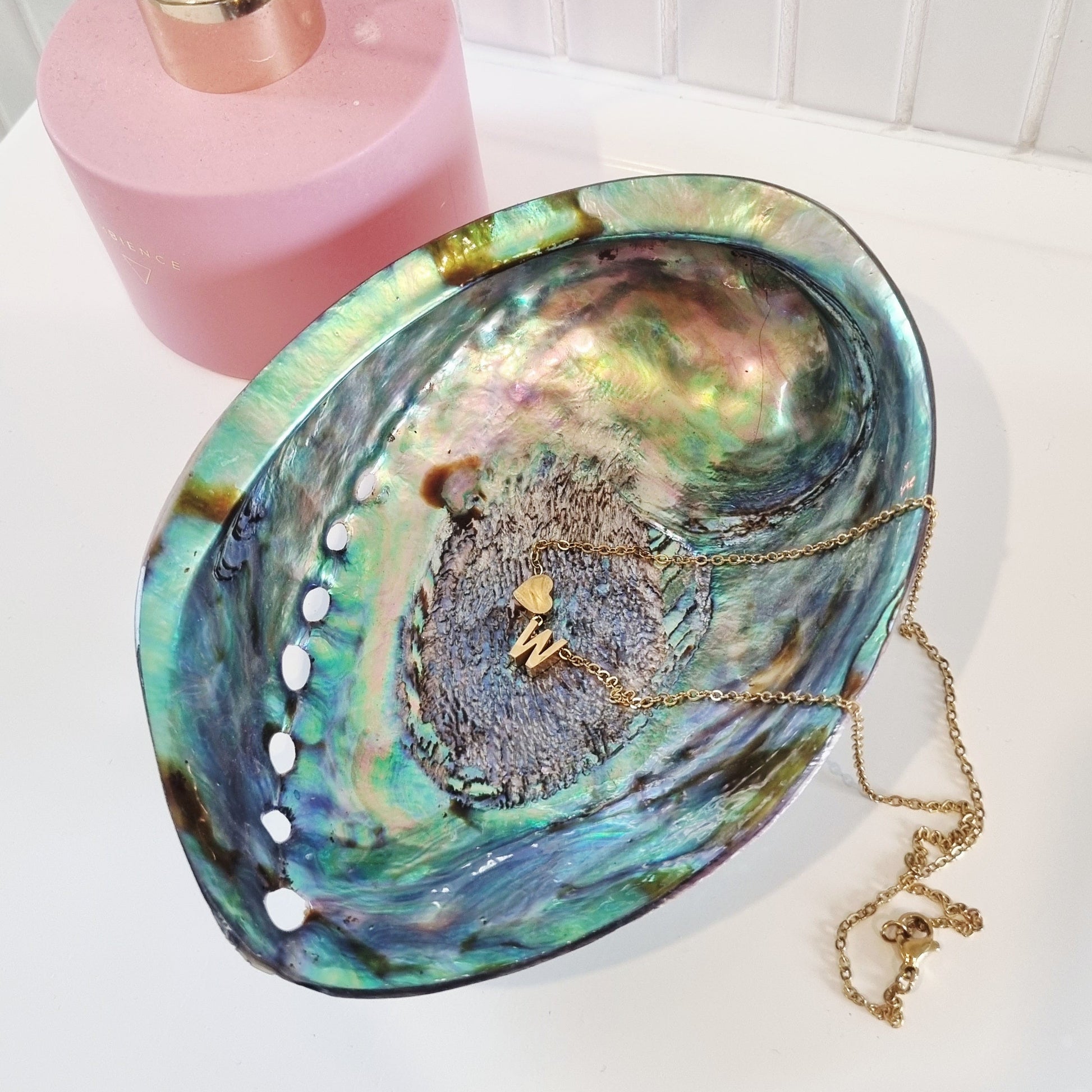 Jewelry dish made from a paua shell with a pink diffuser in the background. Inside the dish is a Love Letter Necklace from Dolly & Naana