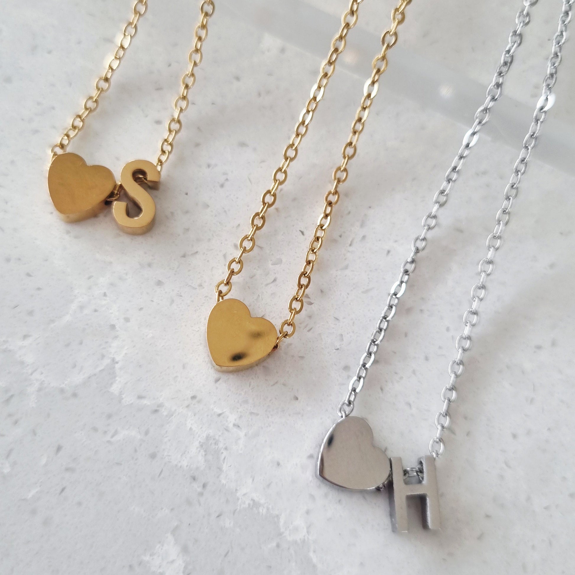 Three necklaces with small love letter charm pendants on a light gray background. Necklaces are gold and silver. 