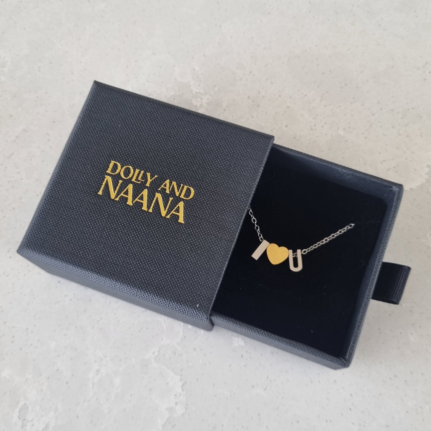 Silver Necklace with a gold heart love letter charm pendant in a 'Dolly and Naana' branded box on a light gray background