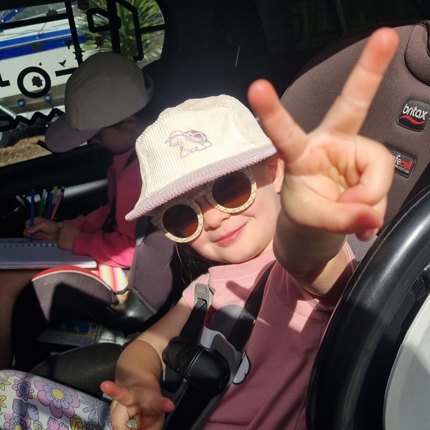 Person sitting in a car seat with sunglasses on, surrounded by colorful patterns.