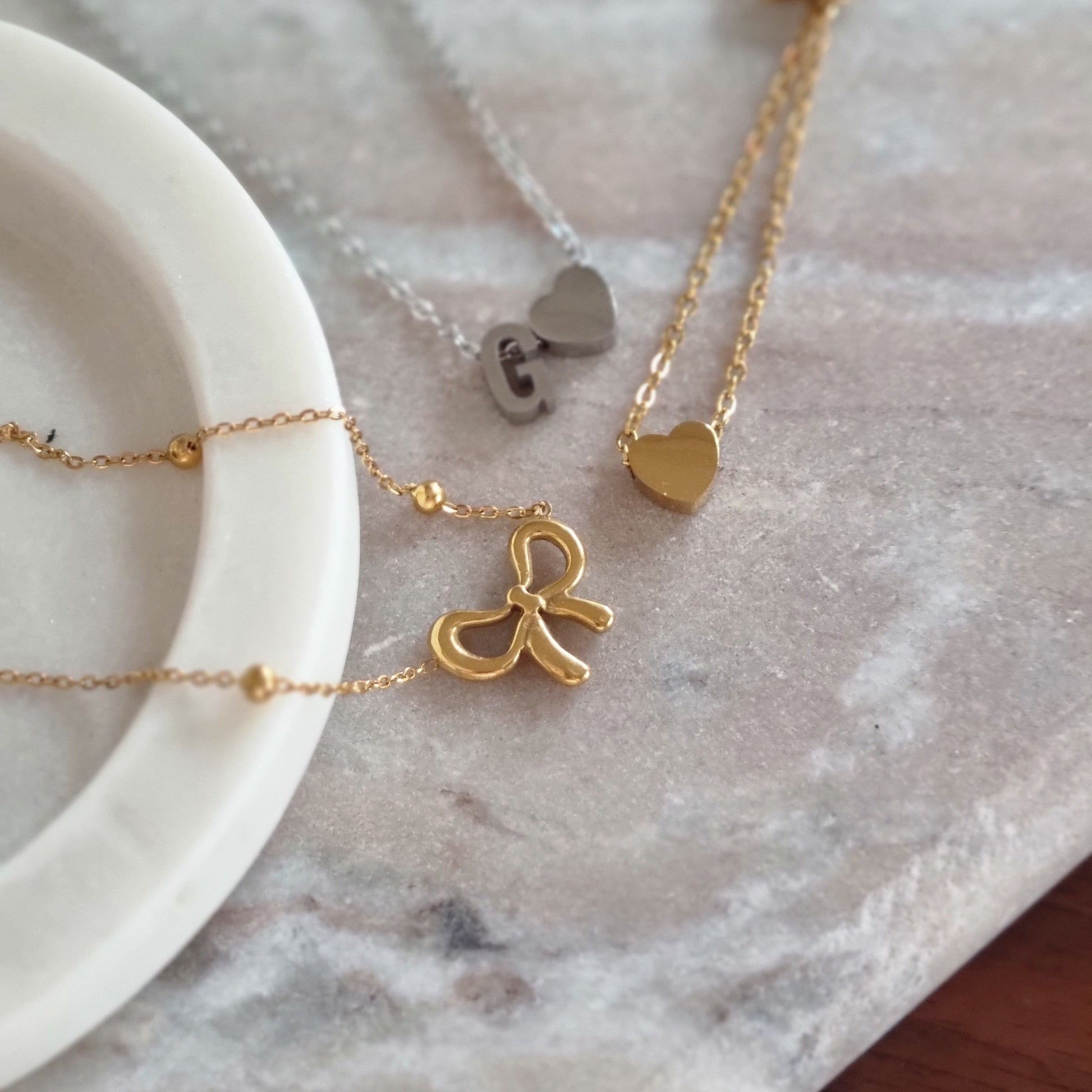 Gold necklaces with heart and bow pendants on a marble surface