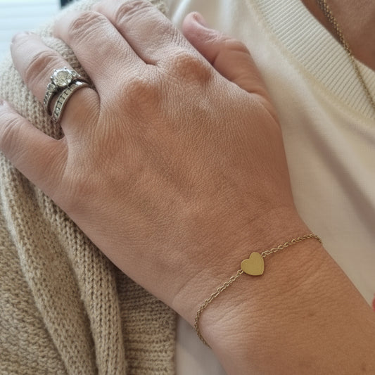 Close-up of a person's hands with jewelry, wearing a beige garment with red text.