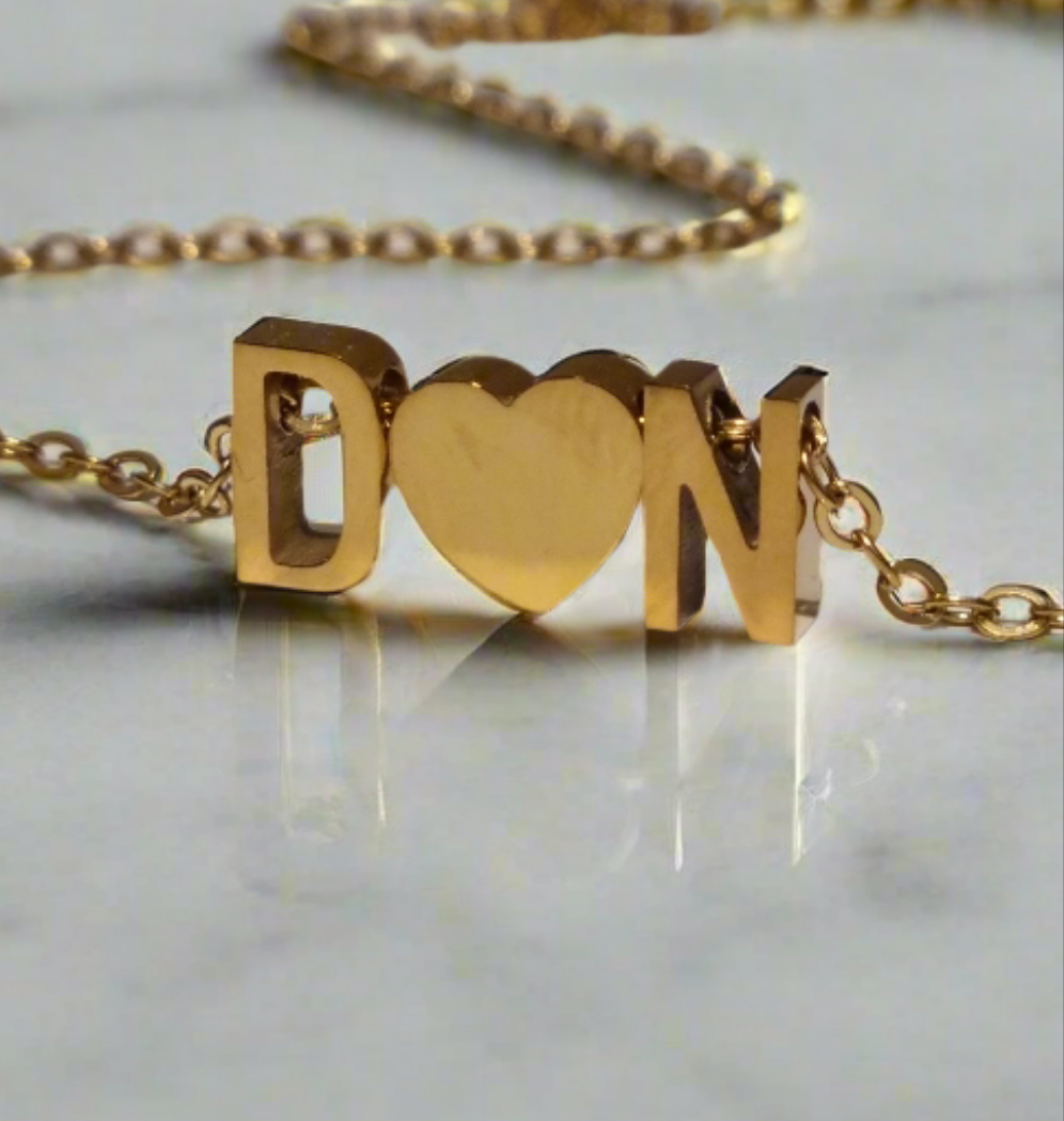 Gold necklace with 'D HEART N' love letter charms on a light background