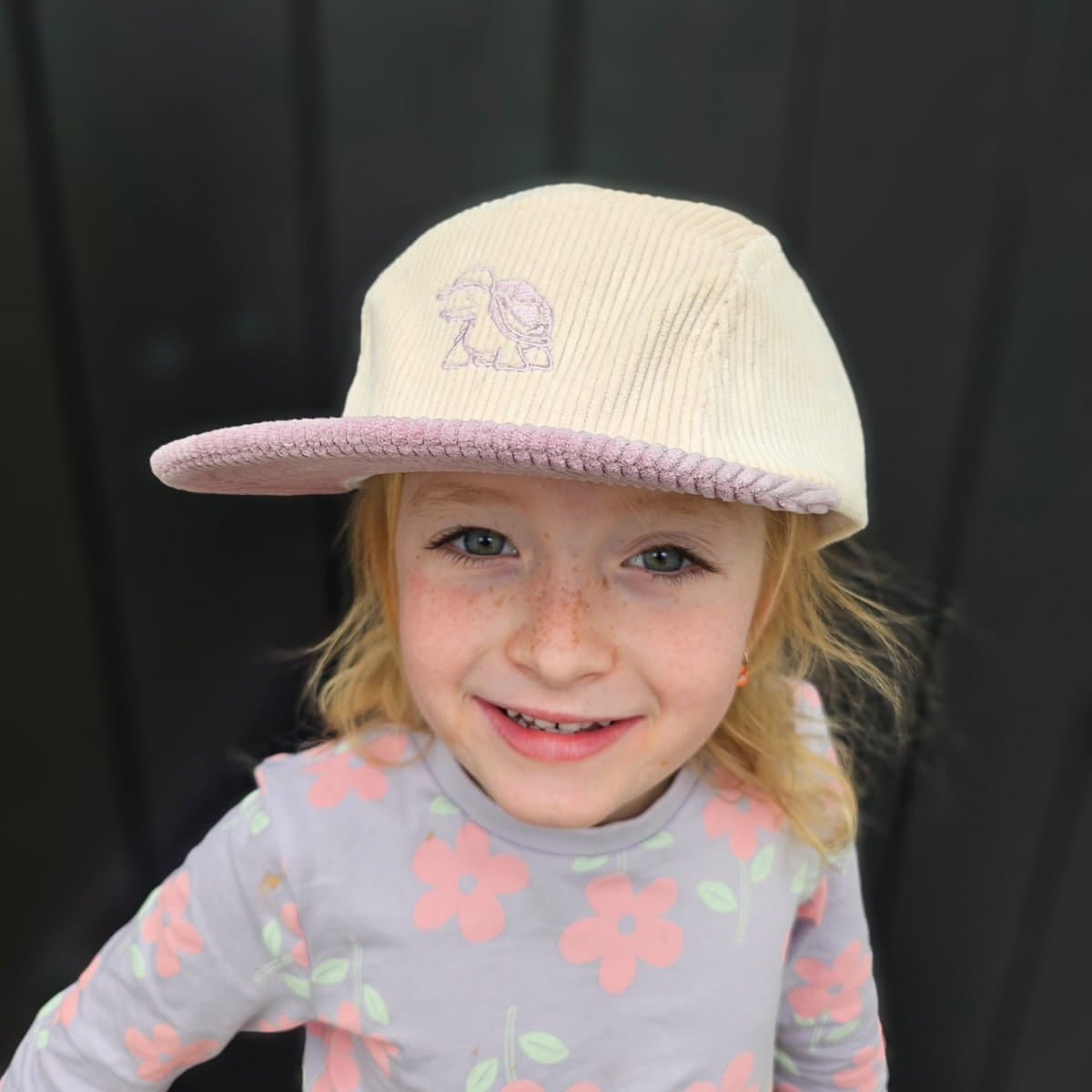 Child wearing a beige cap with a logo against a black background