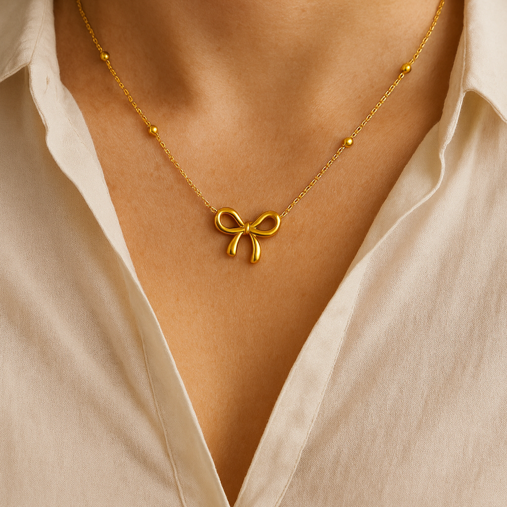 Gold necklace with a bow pendant worn by a person in a light-colored shirt.